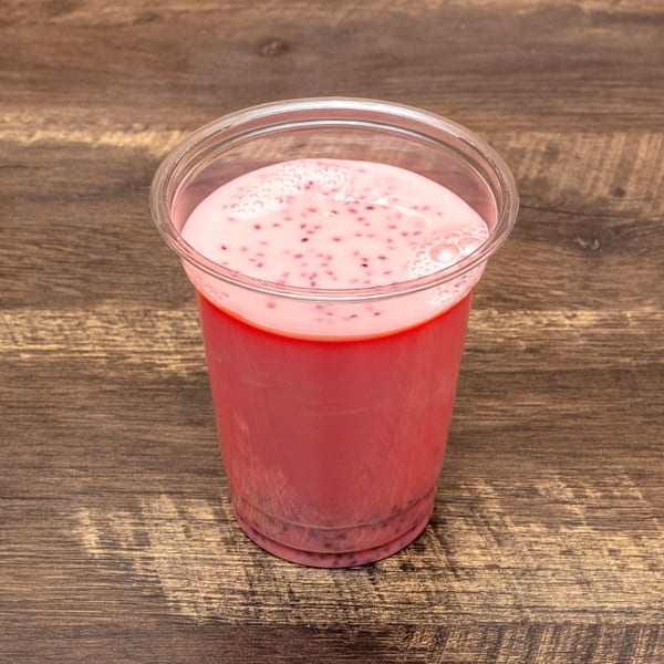 Pink falooda drink with black chia seeds and foam in a clear plastic cup on a wooden table.