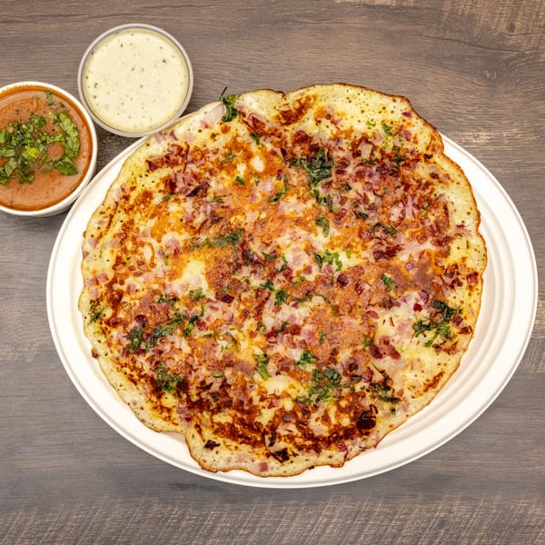 Dosa Spot's onion uttapam, a savory Indian pancake, served with two bowls of chutney.