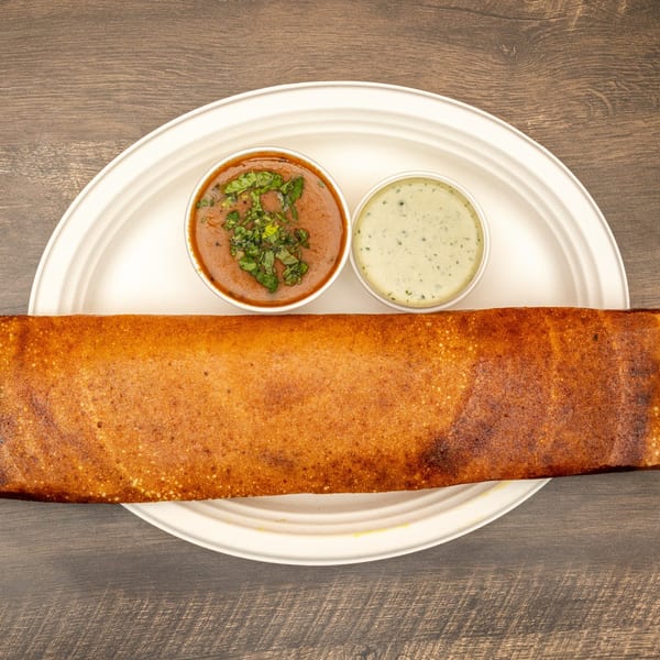 A golden-brown Dosa with two small bowls of chutney and sambar on a white plate.