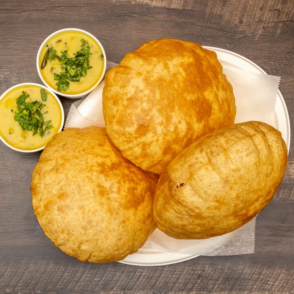 Three golden-brown Indian puri breads on a white plate with two bowls of yellow curry.