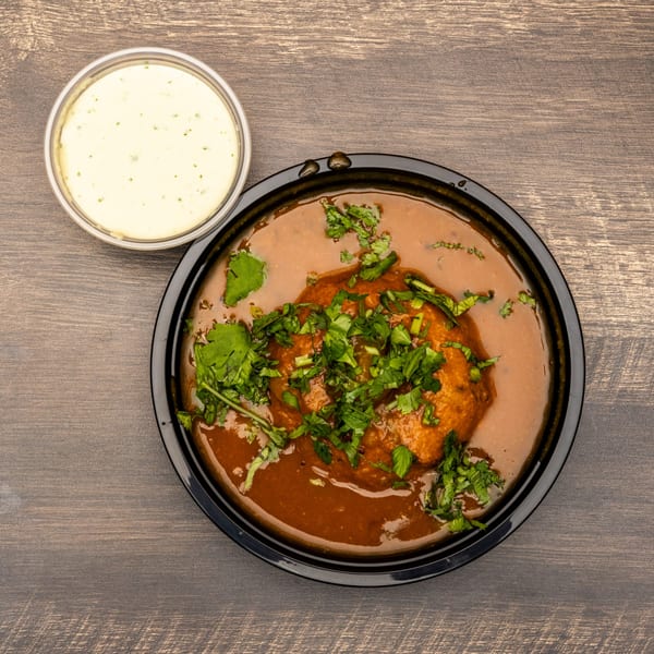 Indian dish with brown gravy, topped with cilantro, and a side of white sauce.