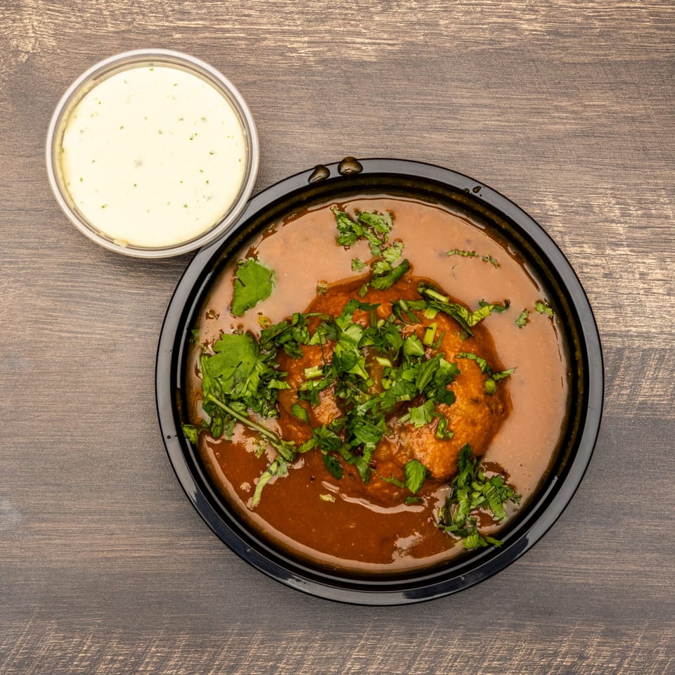 Indian dish with brown gravy, topped with cilantro, and a side of white sauce.